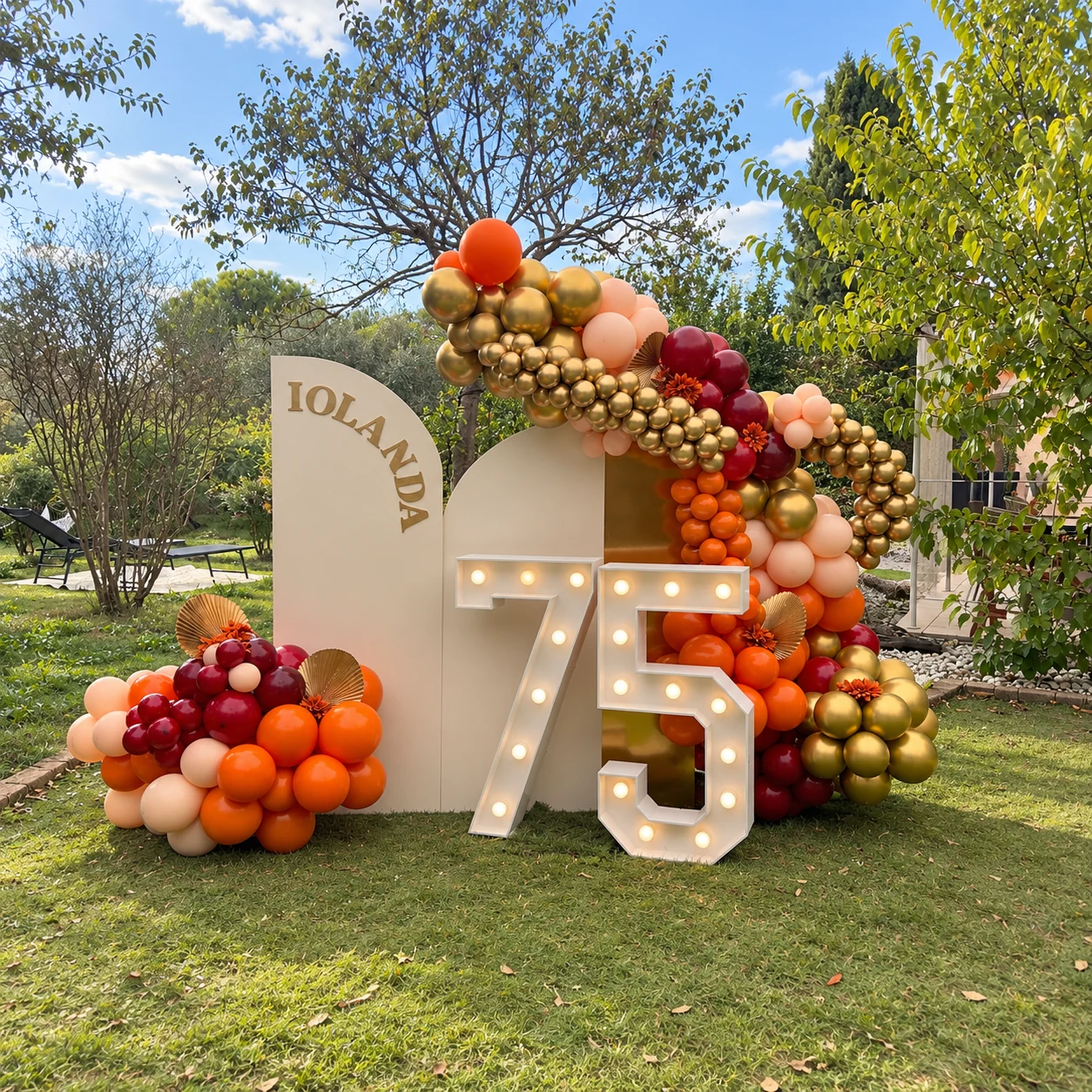 Décor des 75 ans d’Iolanda au jardin avec panneaux crème, ballons automnaux et chiffres 75 allumés
