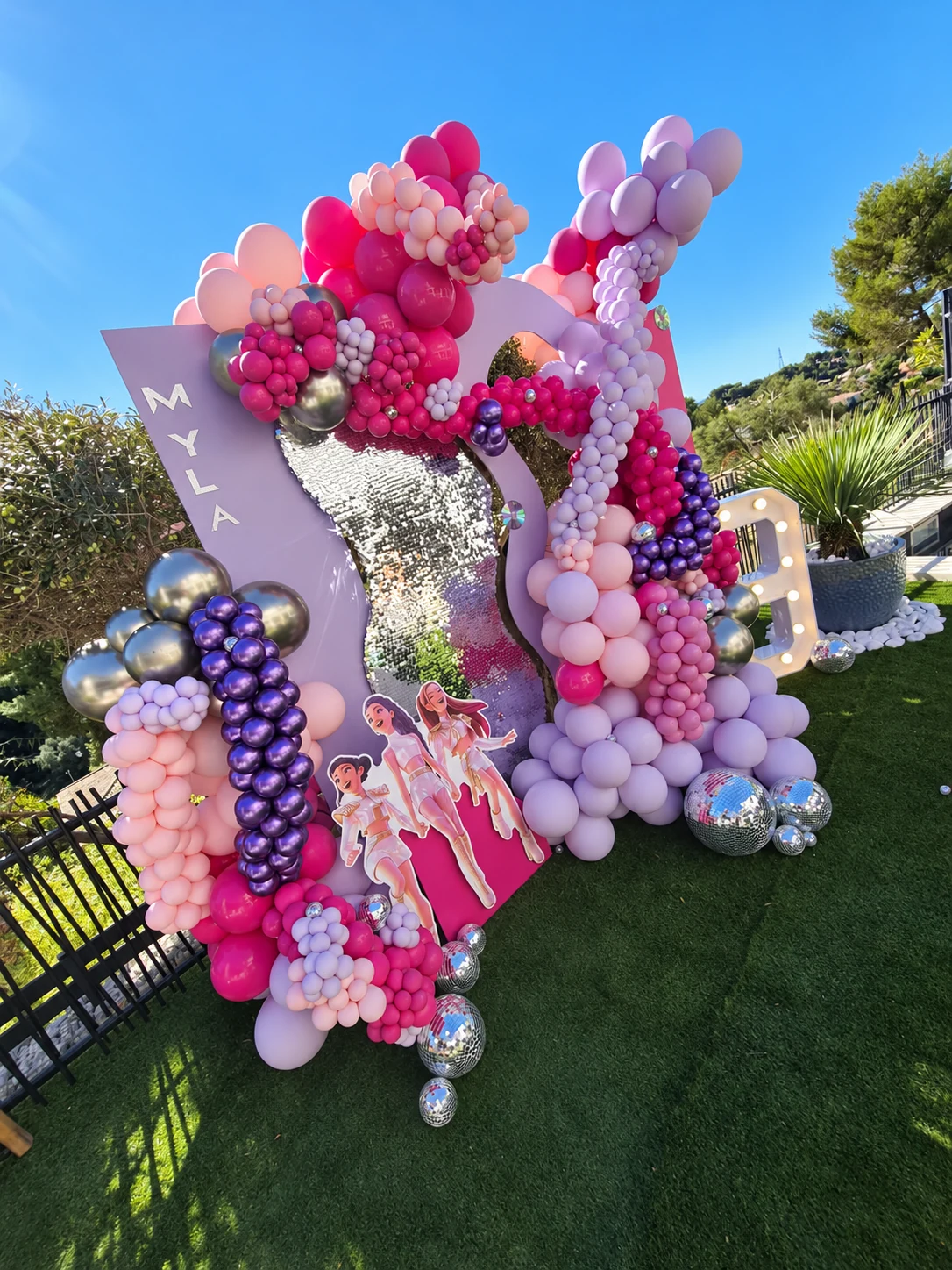 Vue de côté du décor K-pop de Myla avec panneaux roses et lilas, ballons et personnages