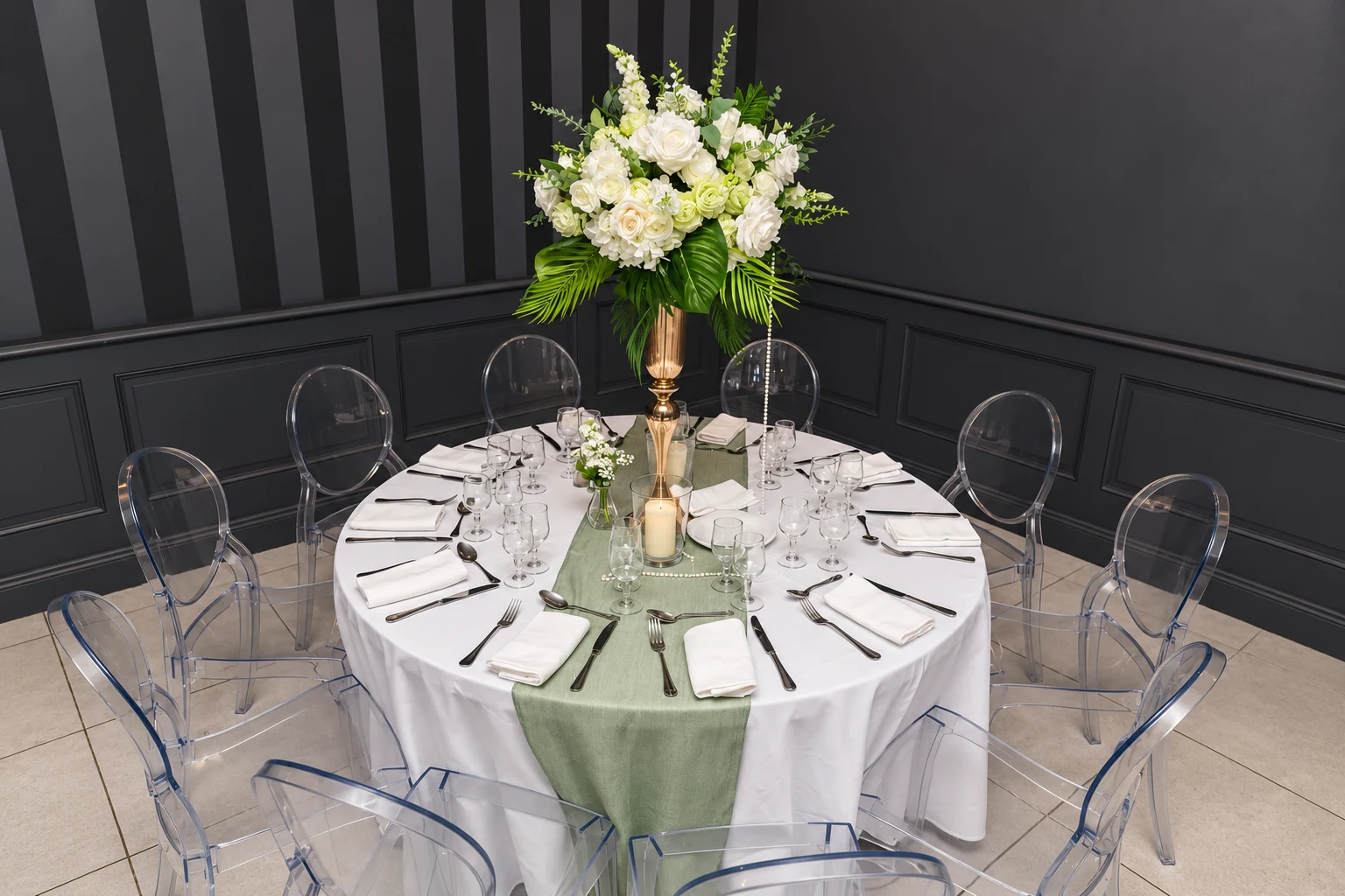 Vue de la table ronde dressée pour l’anniversaire de Nicole, avec chaises transparentes et centre de table fleuri