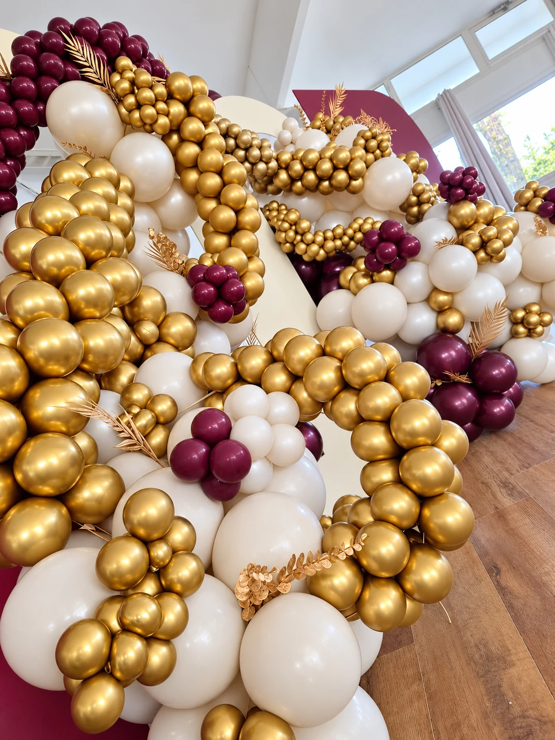 Gros plan sur une composition organique de ballons dorés, ivoire et bordeaux